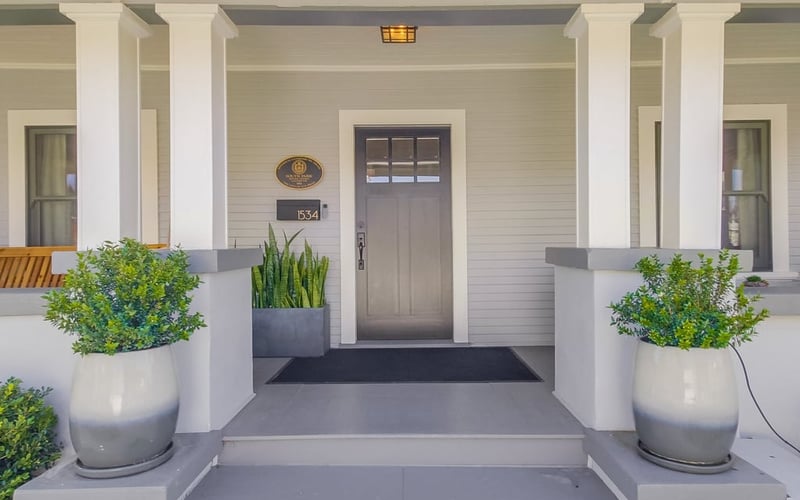 Covered Craftsman front porch with white columns, a grey front door and potted plants flanking the steps