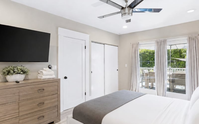 Bedroom with a wall-mounted TV, wood dresser, ceiling fan and a sliding door to a private deck