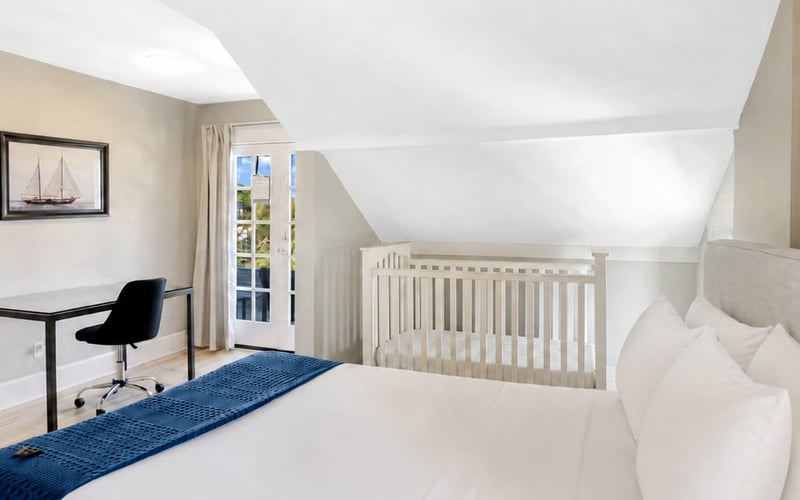 Upstairs bedroom with a desk and chair, a crib in the corner and French doors letting in daylight