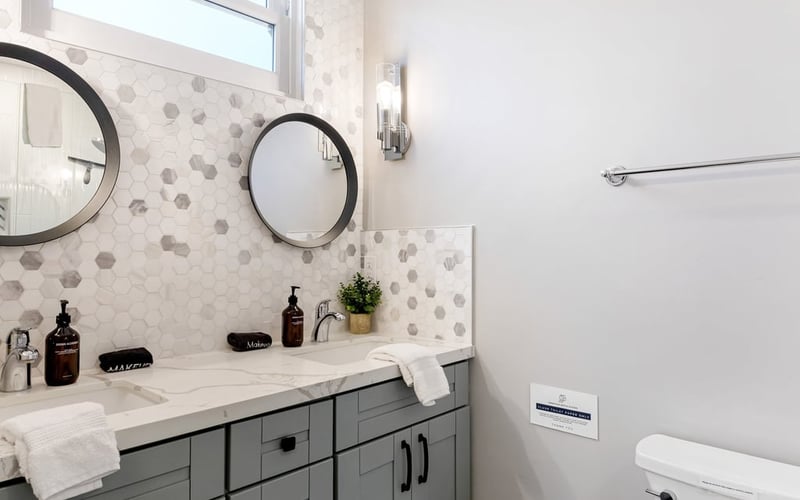 Bathroom with a double vanity, two round mirrors, hexagon tile backsplash and folded white towels