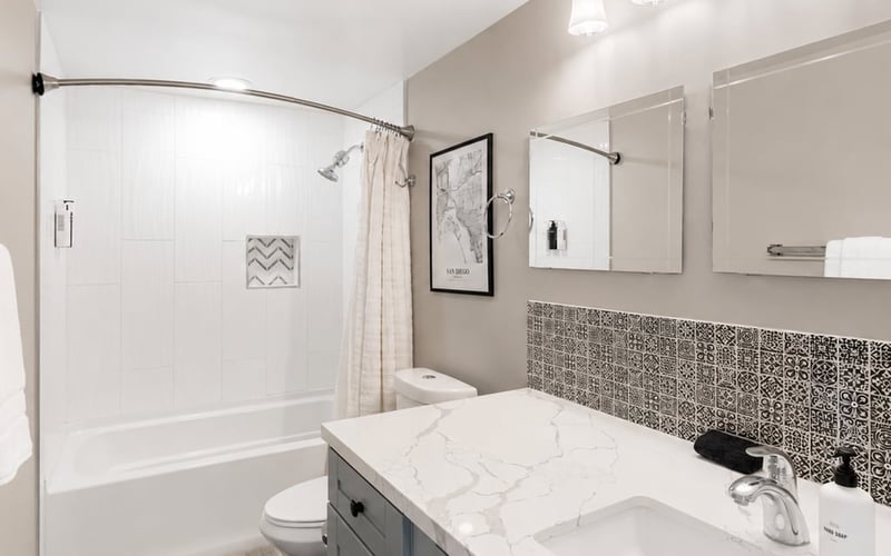 Tiled bathroom with a shower-tub combo, mosaic tile backsplash and a marble-topped vanity