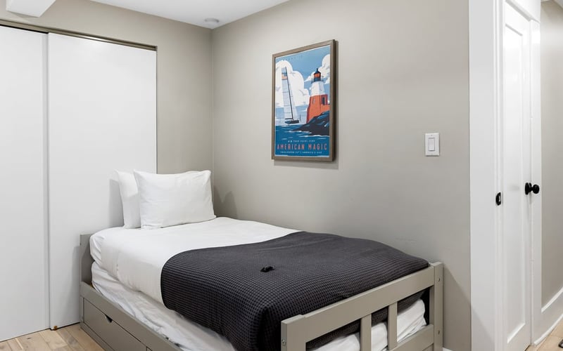 Twin bedroom with a storage bed, grey blanket, closet doors and a framed sailing poster