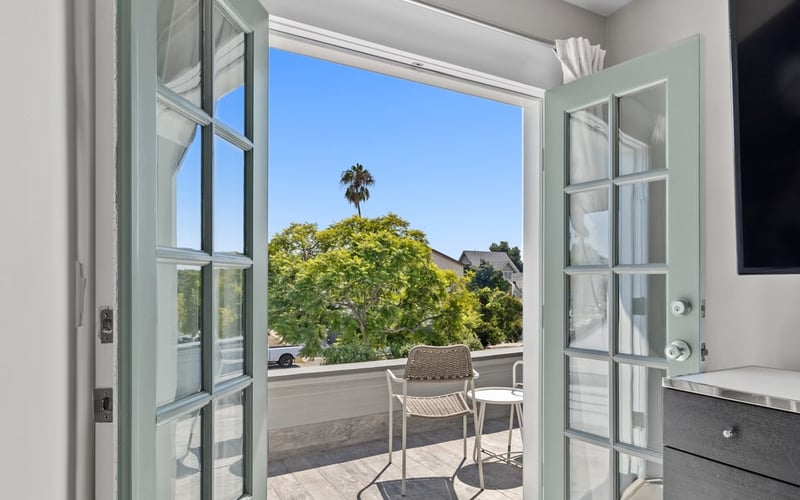 Open French doors leading to the upstairs balcony, with bistro seating and a palm tree beyond