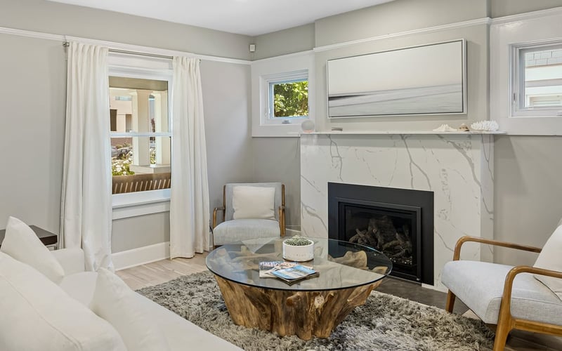 Living room fireplace with a marble surround, white sofa, driftwood coffee table and plush area rug