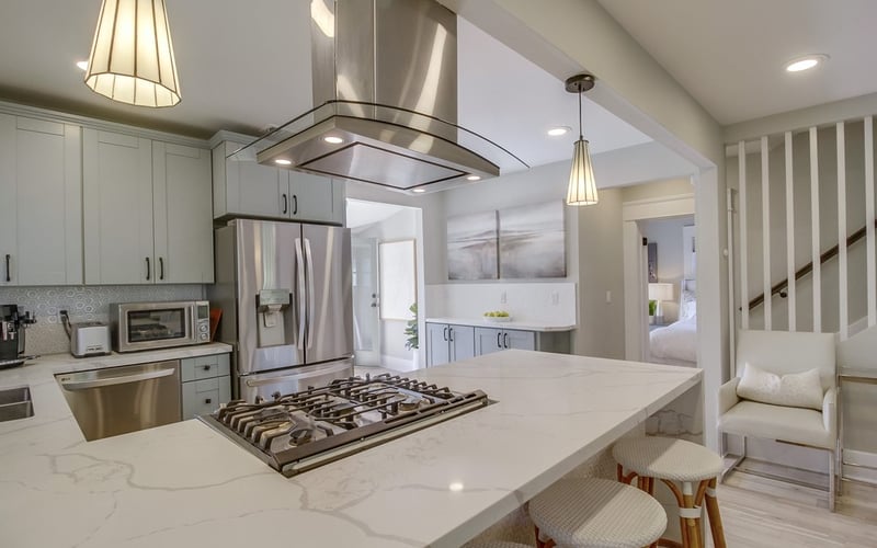 Chef's kitchen with a large quartz island, gas cooktop, stainless range hood and counter stools