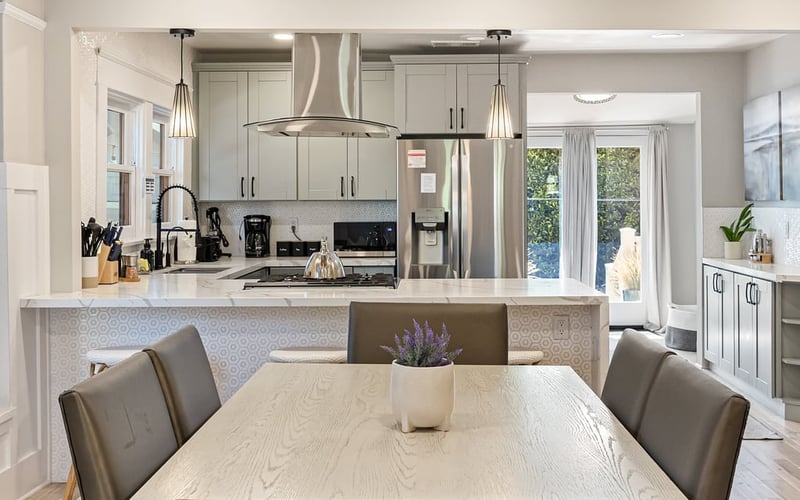 Dining table with leather chairs in front of the kitchen island, pendant lights and stainless appliances