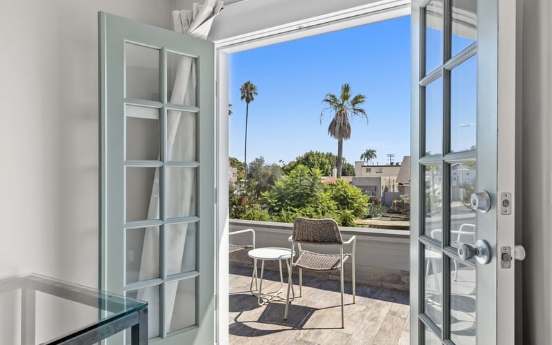 French doors opening onto the upstairs balcony, framing palm trees and rooftops under a blue sky