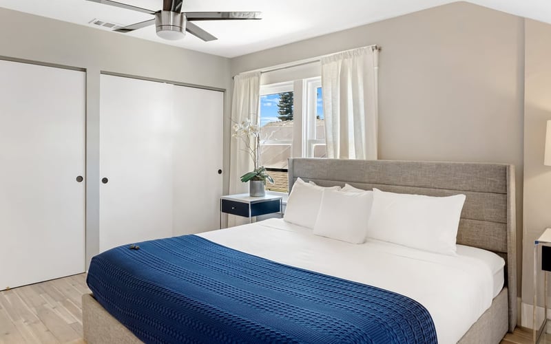 Bedroom with a navy blanket over white bedding, an upholstered headboard, ceiling fan and closet doors