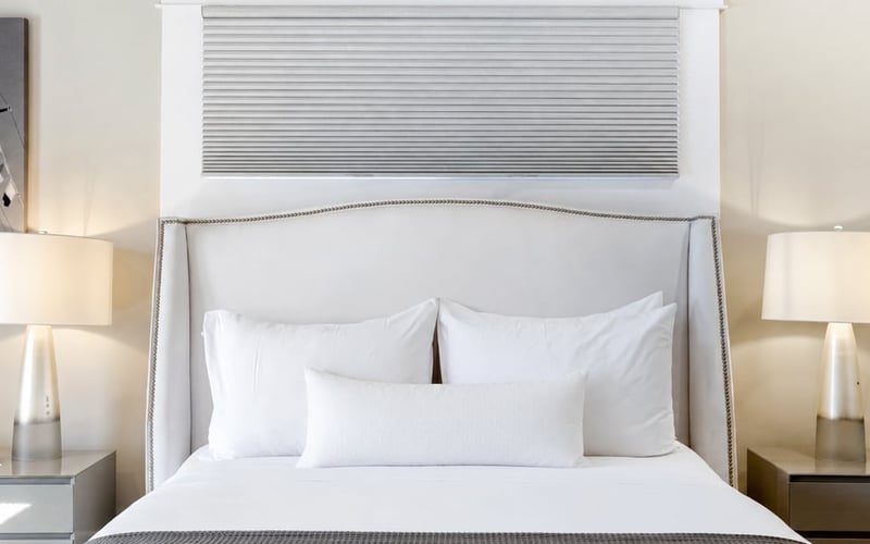 Queen bedroom with an upholstered headboard, white bedding, a grey throw and matching bedside lamps