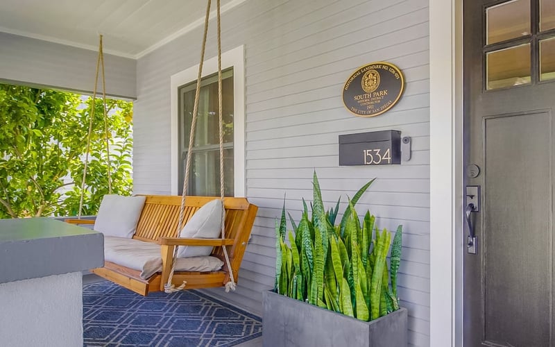 Front porch seating area with a hanging swing, patterned rug and a planter of snake plants beside the front door