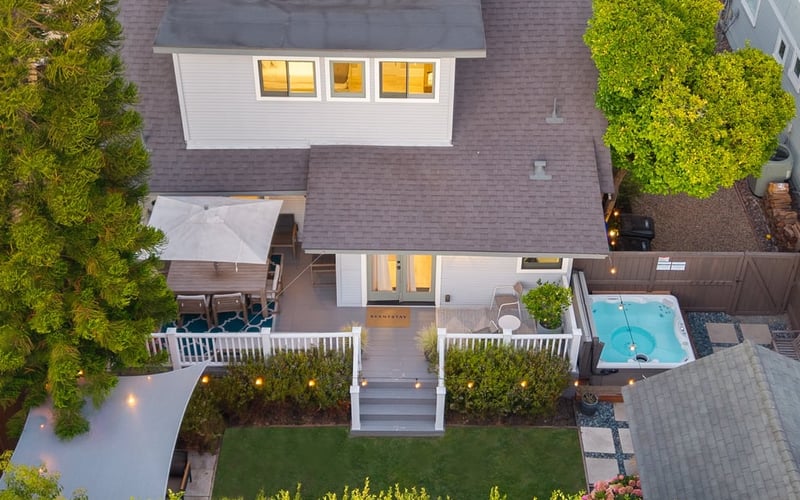Bird's-eye view of the house and backyard at dusk, with lit windows, lawn and a turquoise hot tub